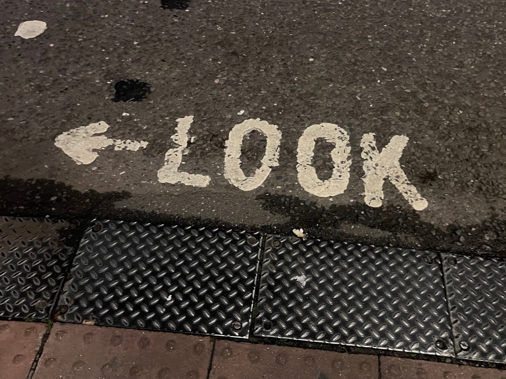 A close up of a pedestrian crossing with a left pointing arrow and the word look written on the floor. 