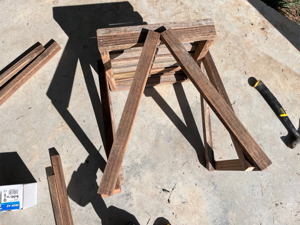 The stool is lying on its side with the A-shaped legs balanced in place ready to be screwed on