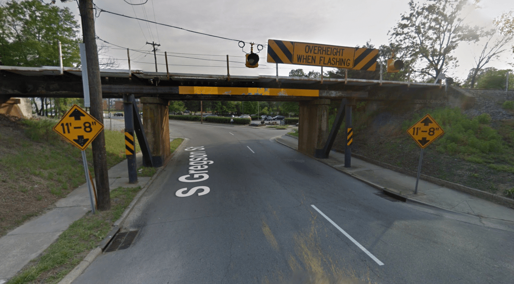 A screen shot from Google Streetview of a road with a bridge running over it, with warnings signs and chevrons on both sides and above the bridge 
