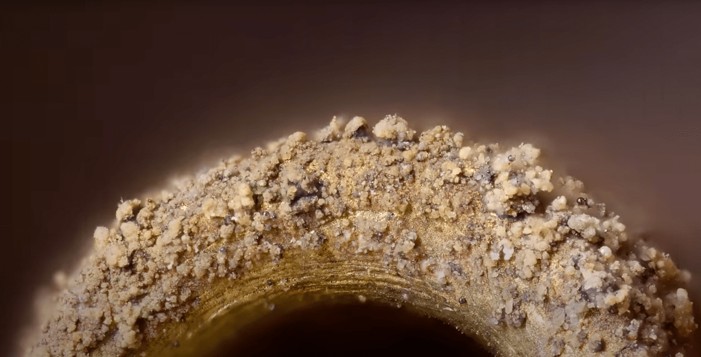 What looks like a car type covered in  golden or brass mud and stones, is actually the microscopic grains of combusted residue that have collected abound one side of the rim of the tiny lighter flame exit hole. 